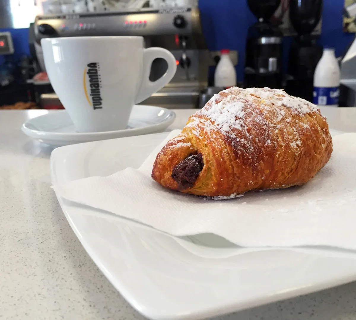 Cafè en tassa blanca i un croissant de xocolata a la barra