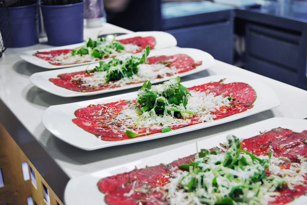 Quatre plats de carpaccio de bou amb parmesà i ruca, a punt de servir