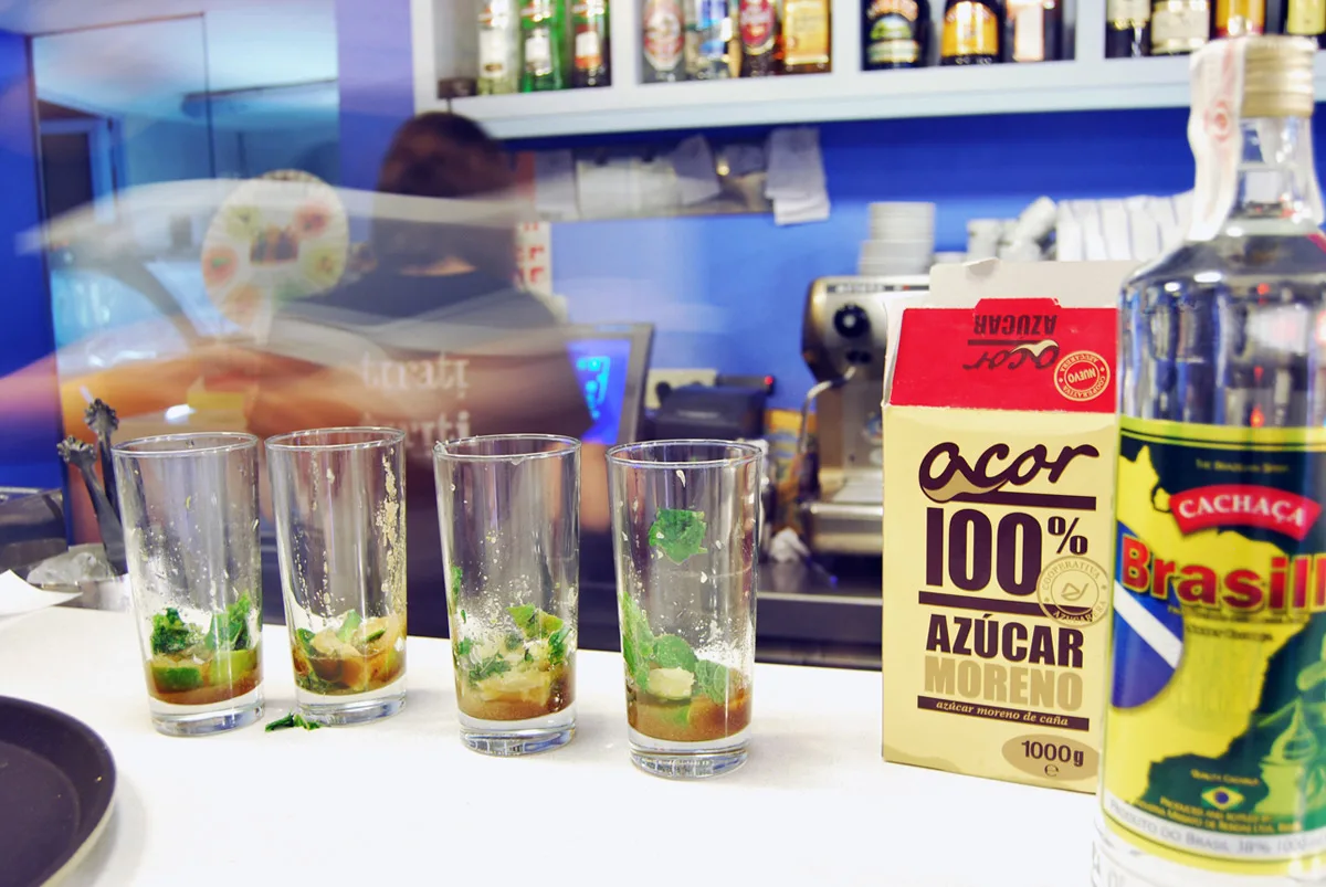 Gots de mojito amb menta i sucre a la barra, al costat d'una ampolla de cachaça