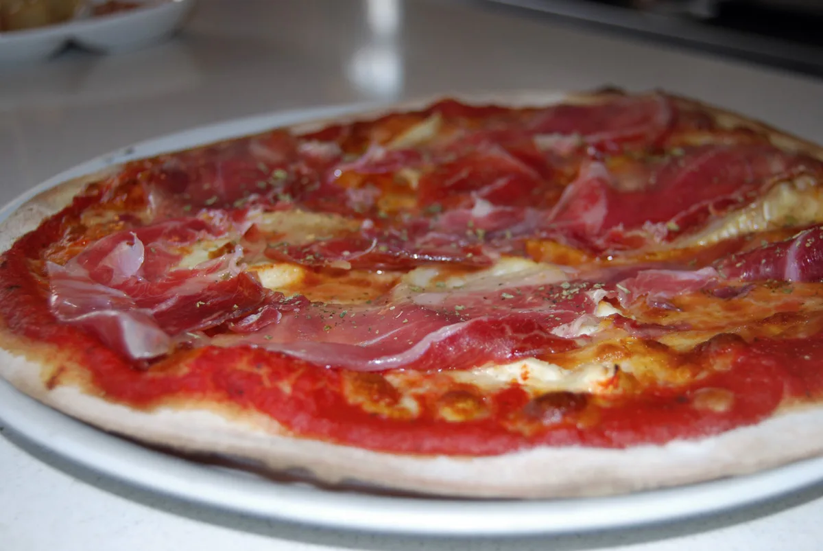 Pizza de tomàquet i mozzarella coberta de pernil, vista de prop