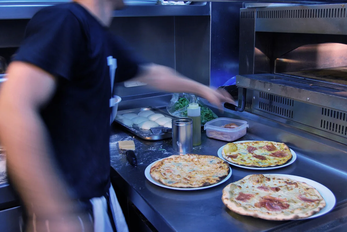 Pizzer preparant pizzes a la cuina, amb tres bases ja amb tomàquet i formatge